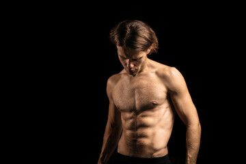young sexy muscular man with a naked torso on a dark background. Long-haired man sportsman.