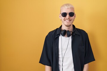 Young caucasian man wearing sunglasses standing over yellow background winking looking at the camera with sexy expression, cheerful and happy face.