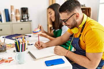 Young hispanic couple smiling happy drawing sitting on the table at art studio.