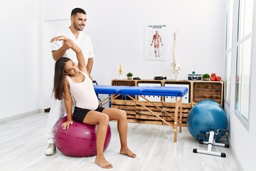 Latin man and woman wearing physiotherapist uniform having pregnancy rehab session using fit ball...