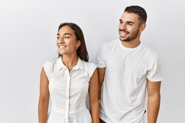 Fototapeta premium Young interracial couple standing together in love over isolated background looking away to side with smile on face, natural expression. laughing confident.