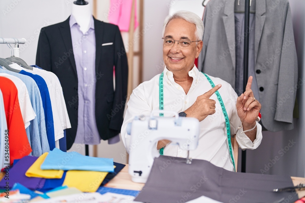 Sticker middle age man with grey hair dressmaker using sewing machine smiling and looking at the camera poin