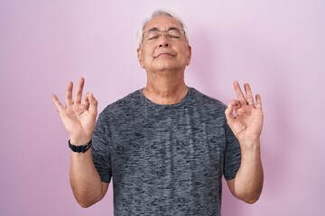 Middle age man with grey hair standing over pink background relaxed and smiling with eyes closed doing meditation gesture with fingers. yoga concept.