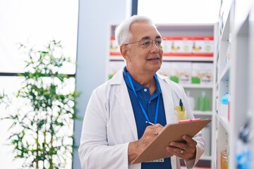 Naklejka na ściany i meble Middle age grey-haired man pharmacist writing on document at pharmacy
