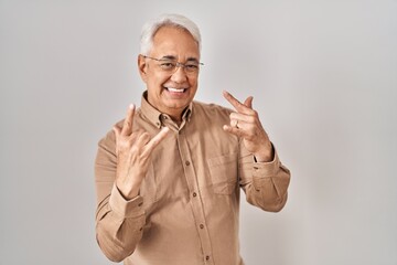 Hispanic senior man wearing glasses shouting with crazy expression doing rock symbol with hands up. music star. heavy concept.