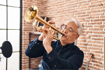 Senior man musician playing trumpet at music studio - obrazy, fototapety, plakaty