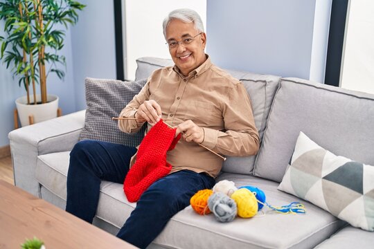 Senior Man Sitting On Sofa Sewing At Home