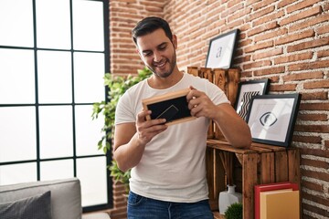 Fototapeta premium Young hispanic man looking photo standing at home