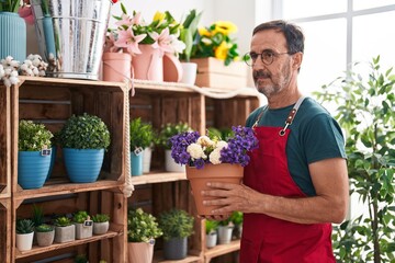 Middle age man florist holding plant of shelving at florist