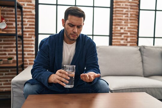 Young Hispanic Man Taking Pills Sitting On Sofa At Home