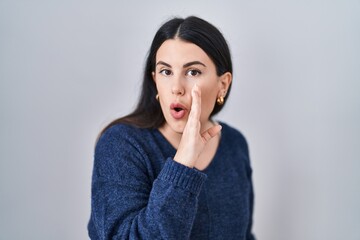 Young brunette woman standing over isolated background hand on mouth telling secret rumor, whispering malicious talk conversation