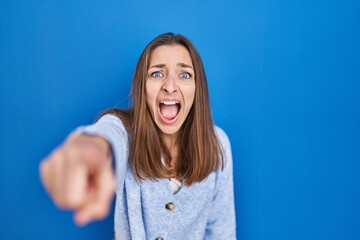 Young woman standing over blue background pointing displeased and frustrated to the camera, angry...