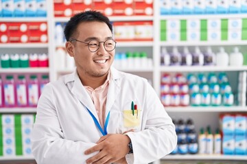 Chinese young man working at pharmacy drugstore looking away to side with smile on face, natural expression. laughing confident.