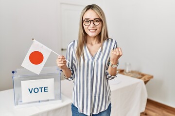 Asian young woman at political campaign election holding japan flag screaming proud, celebrating victory and success very excited with raised arms