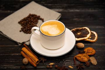 A mug of coffee on a wooden background with spices.