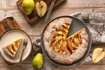 Autumn baking: homemade pear pie and ripe pears on a light wooden table. Open pie with pears and caramel. Photo in rustic style.