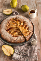 Autumn baking: homemade pear pie and ripe pears on a light wooden table. Open pie with pears and caramel. Photo in rustic style.