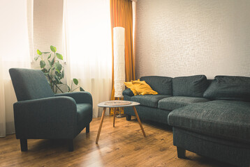 Cozy apartment living room with sofa and yellow pillows and stylisg table with book by flower and window with blue light outside in winter. Grey armchair .opy paste wall background
