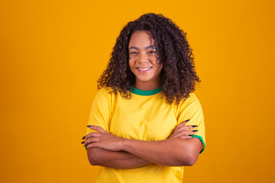 Young black Brazilian, soccer fan. arms crossed over the body. Beautiful brazilian cheerleader with arms crossed on yellow background