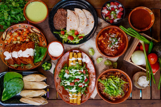 Mesa mexicana con menudo, pozole, enchiladas, tacos, salsa pico de gallo, flautas y tamales