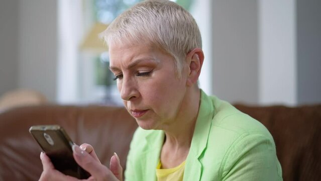 Middle aged woman squinting looking at smartphone screen in slow motion. Portrait of Caucasian grey-haired businesswoman with poor eyesight reading online message in phone application