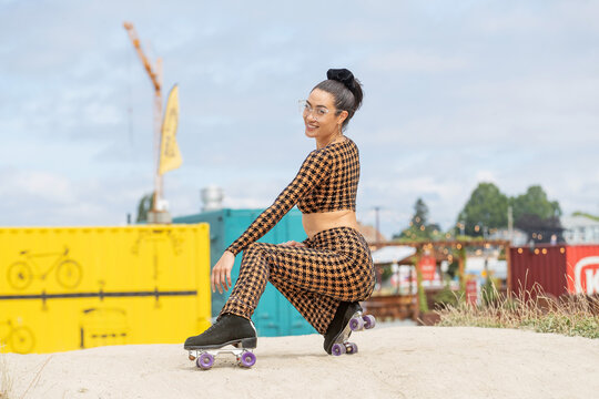 Asian woman on dirt hill wearing roller skates and a tight fitting, two piece body suit with checkered pattern while she is playing outside. 