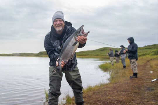 Happy Fisherman Holding Large Coho Salmon On The Bank Of Egegik River In Alaska. 