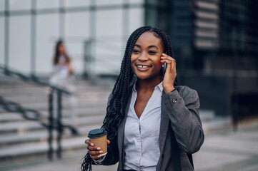 African american business woman outside using a smartphone and drinking coffee