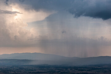 Rain and mist between valley and layers of mountains and hills beneath a moody, overcast sky with heavy clouds