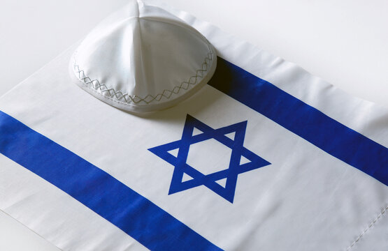 Kippah (religious Hat) With The Flag Of Israel In The Background. Still Life Of Jewish Symbols For Sukkot, Shabbat, Rosh Hashanah And  Independence Day. Star Of David, Yarmulke Kippa On Israeli Flag