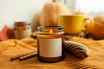 Blank label on a burning candle in autumn decor, space for your logo
