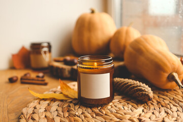 Blank label on a burning candle in autumn decor, space for your logo