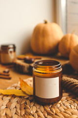 Blank label on a burning candle in autumn decor, space for your logo