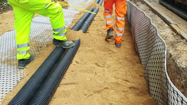 Groundworkers installing new electric ducts during roadworks on construction site 