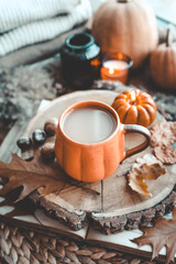 A cup of cocoa and a burning candle and autumn decor on the windowsill
