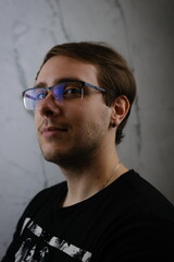 Fototapeta premium Unshorn and unshaven guy in glasses and black tshirt with long hair on gray background