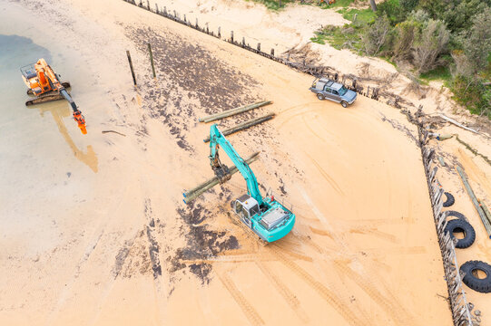 Aerial view  a colourful diggers carrying poles along a sandy beach
