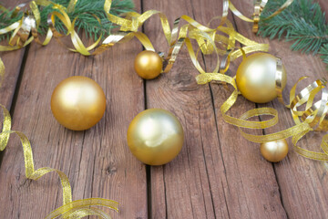 Fototapeta na wymiar Christmas composition of yellow Christmas balls, fir branches, and a gold ribbon on a brown wooden background.
