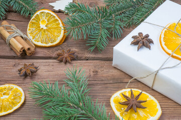 Fototapeta na wymiar Christmas presents or gift box wrapped in kraft paper with decorations, pine cones, dry orange orange slices, cinnamon and fir branches on a rustic wooden background. Holiday concept.