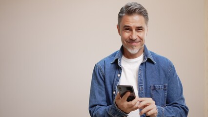 Portrait of happy casual older man with phone, smiling, Mid adult, mature age guy with gray hair,...
