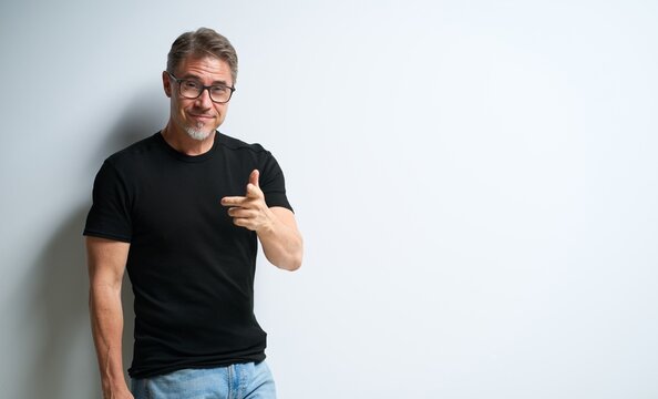 Portrait Of Happy Casual Older Man Smiling, Pointing At You. Mid Adult, Mature Age Guy At White Wall, Isolated On White Background, Copy Space.