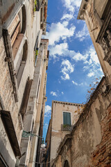 Vintage walls with high windows under blue sky with white clouds in Venice on a sunny morning, wooden shutters on Venetian windows, old buildings, texture of old walls in Venice, view from below