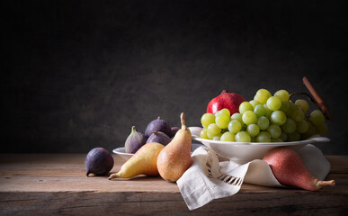 Autumn fruits, grapes, pears, figs and pomegranate on old wooden table, space for text, still life.