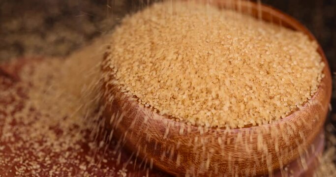 Pour natural brown cane sugar into a wooden bowl, brown sugar is poured on the table and into a wooden bowl
