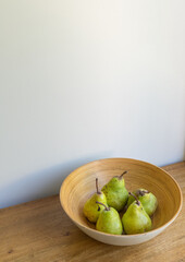Vertical high angle view of organic pears in bamboo bowl on oak table against beige wall (selective focus)