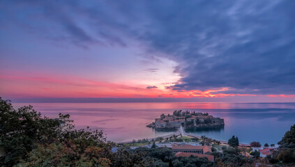 Fototapeta na wymiar Touristic destination Sveti Stefan peninsula with a beautiful colorful sunset and clouds on horizon as a background
