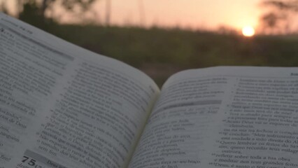 Man holding a bible against the sun in a late afternoon. Man doing prayer outdoors. Man praying at sunset. Holy Bible. Rosary. Religious man. Religion. Prayer in the late afternoon landscape.
