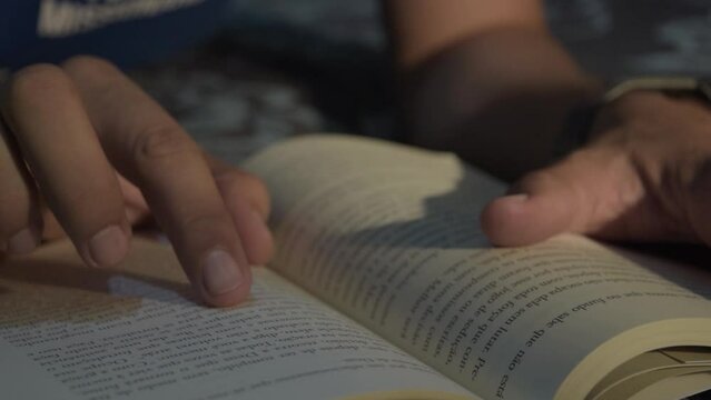 Man reading book in his bed. Reading book before bed. Man swiping his finger on the book page. Night book reading.