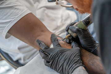Mains d'un tatoueur en train de tatouer sur la peau d'un avant bras - obrazy, fototapety, plakaty
