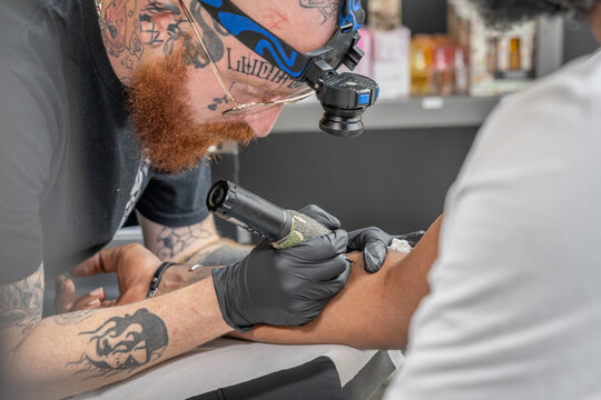 tatoueur roux et barbu en train de réaliser un tatouage flash sur un avant bras